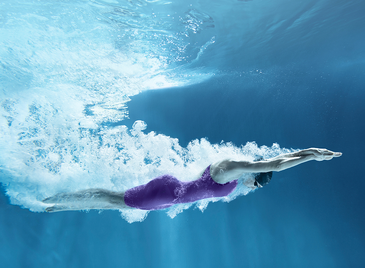 Decorative. Underwater view of a swimmer in a purple swimsuit gliding through clear blue water.