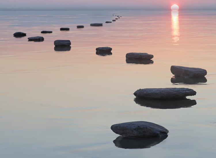 Decorative. Calm water at sunset with a line of stepping stones leading toward the horizon.