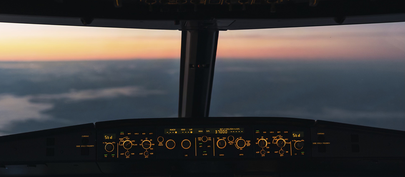 Decorative. Airplane cockpit controls silhouetted against a sunrise above clouds
