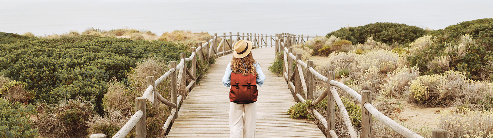 Decorative. Person with a backpack, walking along a wooden boardwalk toward the beach.
